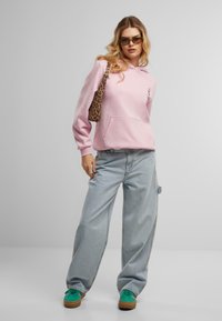Sweatshirt à capuche rose avec poche avant, associé à un jeans baggy bleu clair, des baskets vertes et un sac à épaule en imprimé léopard.