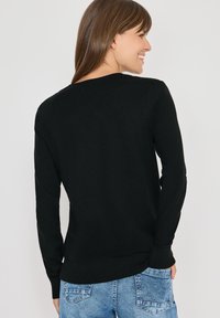Schwarzer, gestrickter Pullover mit langen Ärmeln und rundem Hals. Mit einem gerippten Saum und Bündchen. Kombiniert mit blauen Jeans.