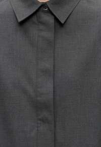 Col de chemise gris foncé avec patte de boutonnage dissimulée et un seul bouton noir visible en haut au centre.
