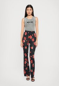 Svarte blomstrete bukser med røde blomster, kombinert med en grå ribbet crop topp med svart skrift. Modellen har på seg svarte sandaler.