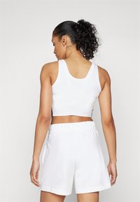 Top cropped blanc et shorts assortis, tous deux en tissu lisse. Le top a des bretelles larges et un design simple.