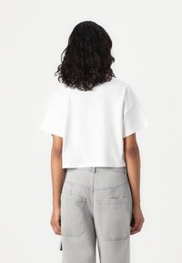 Λευκό κοντομάνικο μπλουζάκι από βαμβάκι σε κομμένο σχέδιο, συνδυασμένο με ανοιχτό γκρίζες ψηλόμεσες παντελόνες που διαθέτουν μεγάλες πίσω τσέπες.