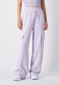 Lichtpaarse cargobroek van zachte stof, met twee zijzakken, een elastische tailleband en een relaxte fit. Witte sneakers maken de look af.