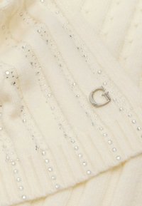 Tessuto lavorato a maglia avorio con decorazioni argentate brillanti disposte in linee verticali, caratterizzato da un piccolo logo metallico.