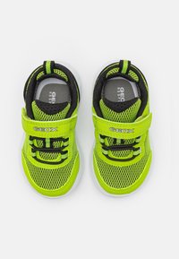 Zapatillas de malla verdes con un interior negro, que presentan una correa de Velcro, cordones y una suela blanca translúcida. Logotipo de la marca visible en el lado.