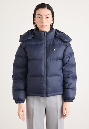Navy blauwe pufferjack met een rits aan de voorkant, hoge kraag en verstelbare manchetten. Logo op de borst, gestikte ontwerp, medium lengte.