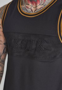 Svart ärmlös tröja med gula detaljer. Har en texturerad framsida med "SIKSILK" broderi. Tillverkad av andningsbart meshmaterial.