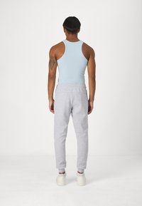Light blue tank top and gray sweatpants view from the back. Tank is fitted, fabric is smooth; sweatpants have an elastic waistband and cuffed ankles.