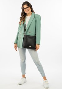 Black leather shoulder bag with textured surface, adjustable strap, and a small metallic logo detail. Worn with a mint blazer and jeans.