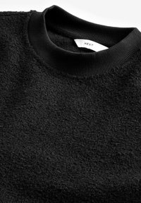 Sort tekstureret sweater med en ribbet sort halsudskæring. Stoffet har en blød, fuzzy tekstur, der viser en let glans i visse områder.