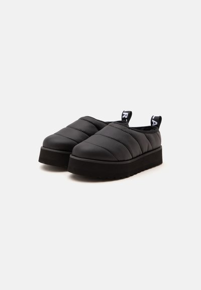 Ζευγάρι μαύρα παπούτσια τύπου slip-on με πάτο πλατφόρμα, μαλακά επενδυμένα καπιτονέ επάνω μέρη και μαύρες θηλιές με λευκά γράμματα.