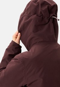 Bordeaux waterdichte jas met een passende capuchon. Kenmerkt zich door een trekkoordsluiting, een gladde textuur en een minimalistisch ontwerp zonder zichtbare logo's.