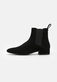 Botines de ante negro con paneles laterales elásticos, punta afilada y tacón bajo. Textura suave y diseño minimalista.