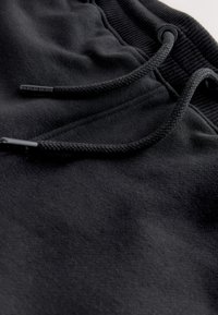 Primo piano del tessuto dei pantaloni della tuta neri che mostra coulisse intrecciate con punte di plastica e vita elasticizzata con occhielli.