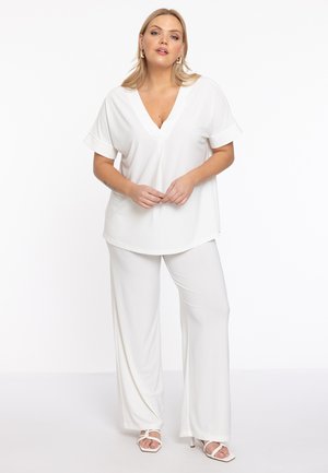 Weißes V-Ausschnitt-Shirt mit kurzen, umgeschlagenen Ärmeln, kombiniert mit locker sitzenden weißen Hosen. Glattes Material mit einer entspannten Silhouette und schlichtem Design.