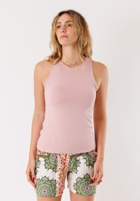 Top in cotone leggero di colore rosa chiaro con un design aderente, realizzato in tessuto liscio. Abbinato a pantaloni shorts con fantasia che presentano accenti verdi e dettagli arancioni.