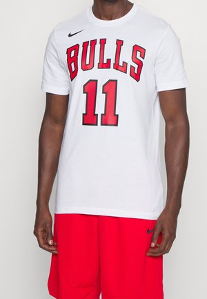 Mann trägt weißes Chicago Bulls T-Shirt mit der Nummer 11 und rote Basketballshorts, steht vor einfachem Hintergrund.