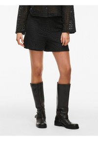 Czarne koronkowe szorty z kwiatowymi wzorami, noszone z czarnymi skórzanymi kozakami do kolan. Całość ma teksturowany, warstwowy wygląd.