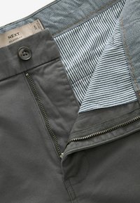 Pantalones grises de corte relajado con cremallera y cierre de botón, que cuentan con una cinturilla interior a rayas y un tejido liso y duradero.