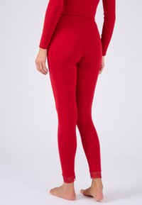 Rote Leggings aus dehnbarem Material mit Spitze am Knöchel. Enganliegendes Design mit hohem Taillenbund und ohne sichtbare Muster.