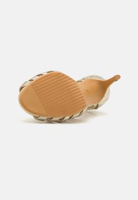 Sandale cu toc transparent, cu talpă bej, având un model texturat și accente din curea metalică. Vedere a tălpii și a părții inferioare a încălțămintei.