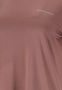 Mjuk mauve-tyg med texten "ENDURANCE" tryckt nära övre högra hörnet, som visar textur och lätta veck av ett plagg.