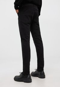 Pantaloni in cotone neri con una vestibilità slim, dotati di tasche posteriori e di una vita testurizzata. Abbinati a scarpe nere con stringhe.