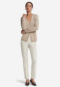 Cardigan lavorato a maglia beige con scollatura a V profonda, abbottonatura frontale e maniche lunghe, abbinato a pantaloni crema e tacchi neri. Design semplice ed elegante.