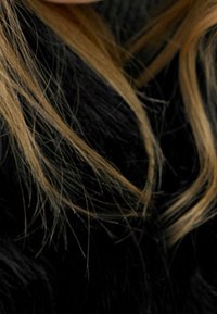 Pitkä, laineikkaat hiukset, joissa on vaaleita raitoja tummemmissa suortuvissa, mustaa taustaa vasten. Tekstuuri näyttää sileältä ja kiiltävältä.