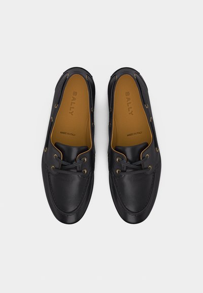 Paire de mocassins loafers noirs en cuir avec détails en lacets et semelles intérieures couleur camel estampillées "BALLY Made in Italy", vues de dessus sur fond blanc.