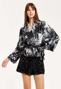 Black and white, floral-patterned shirt with a cinched waist and wide sleeves, paired with a textured black sequined mini skirt.