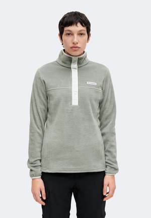 Personne aux cheveux courts et foncés portant un pull polaire léger gris Columbia avec des boutons-pression et un pantalon noir, faisant face à l'avant.