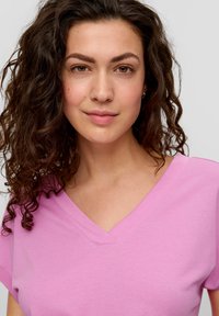 Roze, kortarmige V-hals t-shirt van zachte katoenstof. Beschikt over eenvoudige stiksels en een relaxed fit, zonder aanvullende patronen of accenten.
