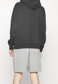 Sudadera con capucha de algodón gris oscuro, de corte relajado, combinada con pantalones cortos gris claro que cuentan con un bolsillo lateral y una textura suave.