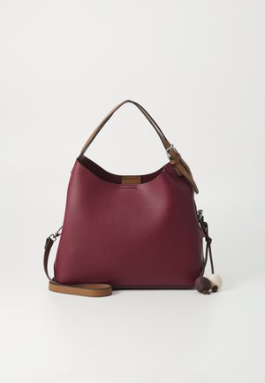 Bolso de mano de cuero burdeos con correa ajustable para el hombro y asa en marrón, con dos pompones decorativos de tela en marrón y beige.