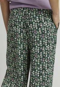 Blommönstrade byxor med en mörkgrön bakgrund, prydda med små rosa, vita och ljusgröna blommor. Mjukt, lätt tyg med fickor.