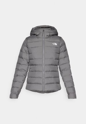 Grijze pufferjack met capuchon, met horizontale stiksels, een rits aan de voorkant en het 'The North Face' logo op de linkerborst.