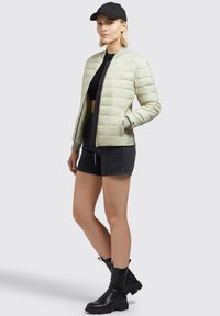 Light green puffer jacket with quilted design, zip closure, and ribbed cuffs. Paired with black shorts and black ankle boots.