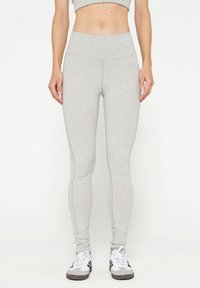 Lichte grijze leggings met een hoge tailleband, een aansluitend ontwerp, een gladde textuur en stikseldetails, gedragen met witte en zwarte sneakers.