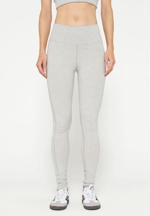Leggings grigio chiaro con un alto punto vita, design aderente, texture liscia e dettagli di cucitura, abbinati a scarpe da ginnastica bianche e nere.