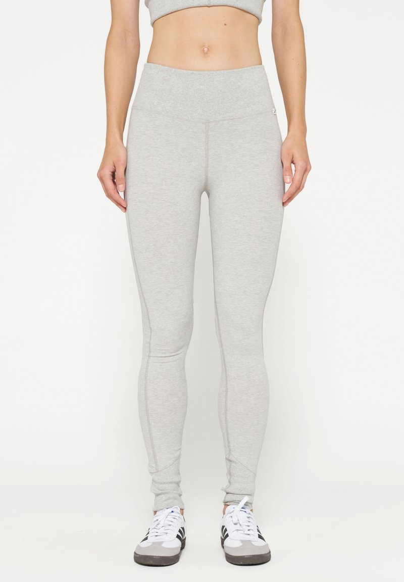 Lichte grijze leggings met een hoge tailleband, een aansluitend ontwerp, een gladde textuur en stikseldetails, gedragen met witte en zwarte sneakers.