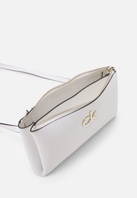 Borsa a tracolla bianca in pelle con chiusura a zip, accessori in oro e bordo nero. Presenta un logo del brand ben visibile sul davanti.