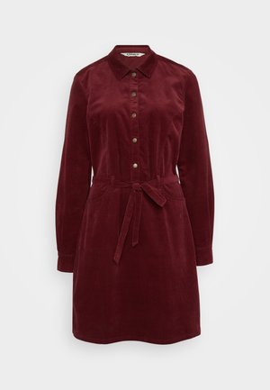 Sukienka koszulowa z korduroju w głębokim czerwonym kolorze, z kołnierzem, przednimi guzikami, długimi rękawami, paskiem w talii i dwiema bocznymi kieszeniami. Miękka tekstura.
