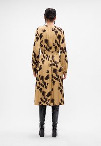 Μπεζ φόρεμα με μαύρο αφηρημένο σχέδιο, μακριά μανίκια, ελαστική μέση και ρευστή σιλουέτα. Φοριέται με μαύρες μπότες μέχρι το γόνατο.