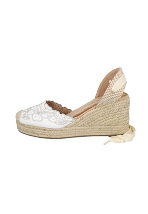Alpargata cuña blanca con bordado floral, suela de yute trenzado y cierre de lazada en el tobillo sobre fondo blanco.