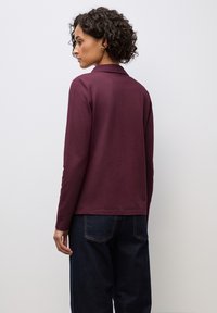 Polo shirt a maniche lunghe color bordeaux con colletto, realizzato in materiale morbido, abbinato a jeans in denim blu scuro. Design semplice senza decorazioni.