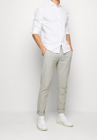 Vit linne knäppskjorta, ljusgrå linnebyxor och vita sneakers. Outfiten har uppvikta ärmar och en avslappnad passform.