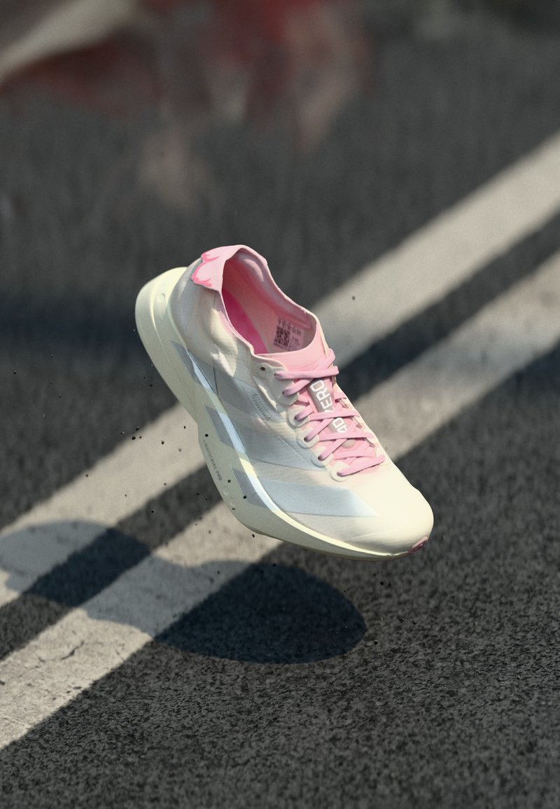 Weißer und pinker Sportschuh in der Luft über einer Asphaltstraße mit weißen Fahrbahnmarkierungen, der einen Schatten darunter wirft.