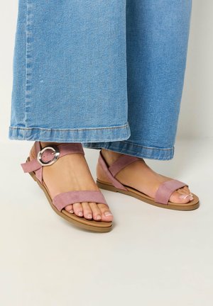 Voeten met roze suède enkelbandjes met zilveren gesp, gecombineerd met lichtblauwe denim jeans met wijde pijpen.