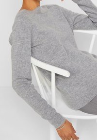 Hellgrauer Strickpullover mit rundem Ausschnitt und langen Ärmeln, mit weicher Textur und taillierter Silhouette.